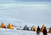 Tents with plane debris in 
        background and helicopter overhead