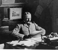 Major Alexander at his desk smoking a pipe