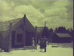 Queen and Guide outside Maori house (whare)