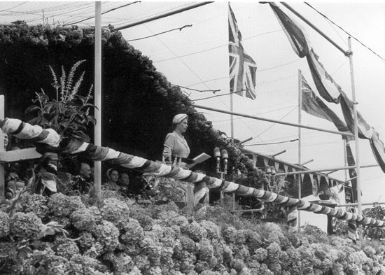 Queen speaking, surrounded by flowers