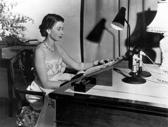 Queen at desk reading to microphone